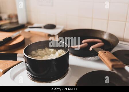 cuisson des aliments sur une cuisinière de cuisine. chou-fleur bouillant au premier plan, saucisses friture en arrière-plan Banque D'Images