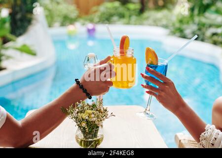 Mains de l'homme et de la femme se clinquant des verres de fruits doux cocktails pour prendre un bain de soleil au bord de la piscine Banque D'Images