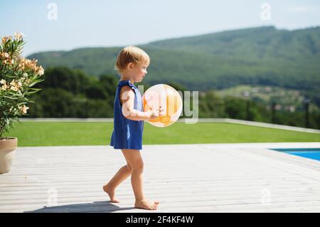Portrait d'une petite fille avec balle marchant à l'extérieur dans le jardin de l'arrière-cour. Banque D'Images