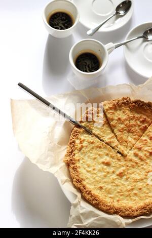 Dessert au fromage coupé en tranches avec deux tasses d'espresso servies sur du blanc. Concept de desserts faits maison. Banque D'Images