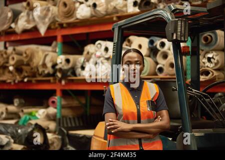 Opérateur de chariot élévateur féminin africain debout dans un entrepôt textile Banque D'Images