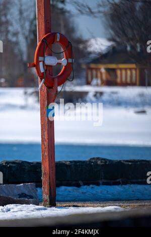 Helsinki / Finlande - 22 MARS 2021 : un gros plan d'un anneau orange de sauvetage suspendu sur un poteau en bois sur le boulevard de la plage. Banque D'Images