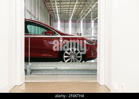 Un modèle X de couleur rouge Tesla est stationné et rechargé à l'intérieur de l'entrepôt de l'usine. Banque D'Images