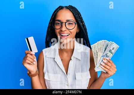 Belle femme hispanique tenant des dollars et de carte de crédit souriant et riant dur dehors fort parce que drôle de blague folle. Banque D'Images
