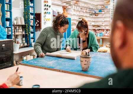 Photo de stock de femmes concentrées dans un tablier travaillant dans un atelier de poterie. Banque D'Images