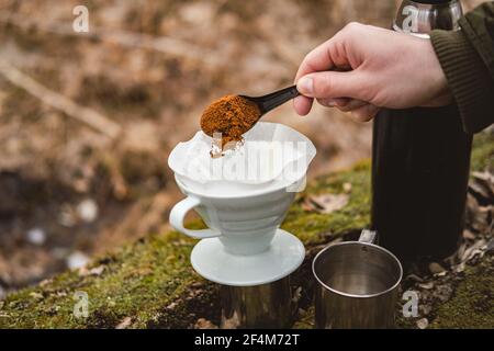 Faire couler le café à l'extérieur lors d'une randonnée. Versez à la main du café moulu dans un filtre en papier pour préparer le café Banque D'Images