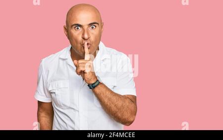 Homme mature du Moyen-Orient avec moustache portant une chemise blanche décontractée demandant à être calme avec le doigt sur les lèvres. Silence et secret concept. Banque D'Images