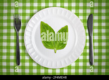 Concept végétalien ou végétarien avec feuilles vertes sur plaque blanche contre le chiffon de table à carreaux verts avec la fourchette et le couteau Banque D'Images