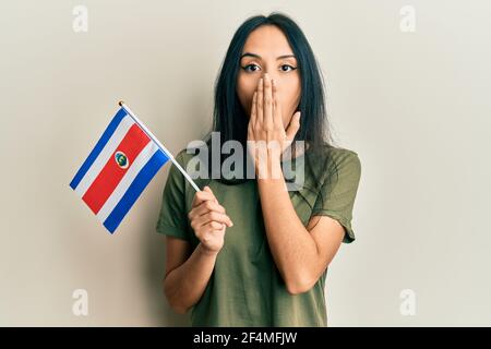 Jeune fille hispanique portant le drapeau du costa rica couvrant la bouche avec la main, choquée et peur de l'erreur. Expression surprise Banque D'Images