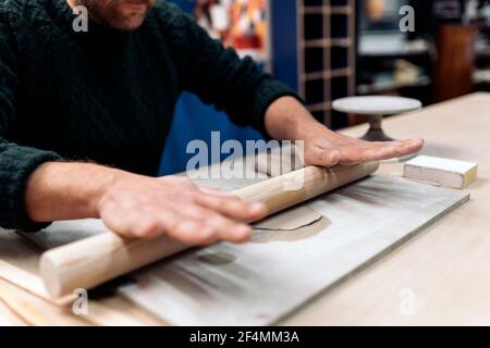 Photo de la personne non reconnue dans le tablier travaillant dans l'atelier de poterie et utilisant l'argile. Banque D'Images