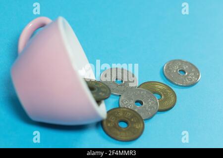 Des pièces en yen japonais débordent d'une tasse de thé rose. Banque D'Images