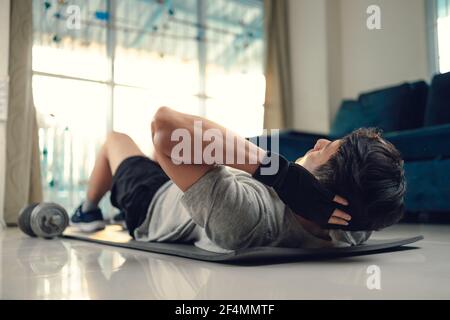 Jeune homme faisant des exercices abdominaux sur le tapis de yoga dans la salle de séjour à la maison. Concept de fitness, d'entraînement et de formation à la maison. Banque D'Images