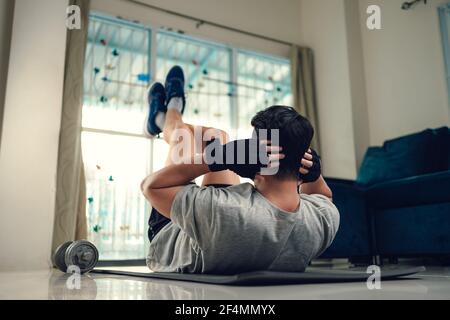 Jeune homme faisant des exercices abdominaux sur le tapis de yoga dans la salle de séjour à la maison. Concept de fitness, d'entraînement et de formation à la maison. Banque D'Images