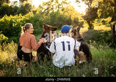 Amour des animaux, entraînement des chiens, meilleures races de chiens pour la famille. Jeunes couples sportifs marchant avec deux chiens de berger allemands en plein air dans le parc d'été Banque D'Images