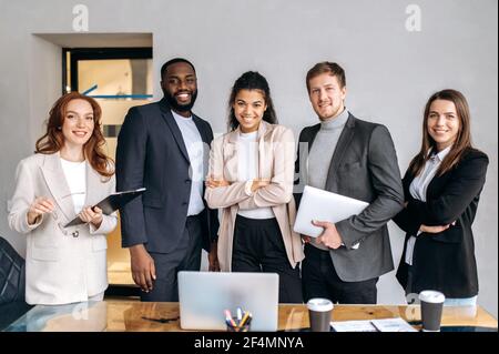 Portrait de personnes influentes dans les bureaux modernes. Les collègues multiethniques qui réussissent dans des costumes élégants regardent directement le concept de caméra, sourire, partenariat Banque D'Images