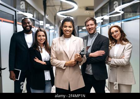 Portrait de partenaires d'affaires élégants et heureux sur le lieu de travail. Femme africaine américaine boss en costume élégant debout au bureau avec ses employés professionnels, regardant la caméra, souriant Banque D'Images