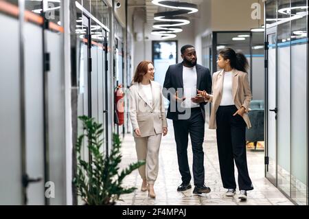 Concentration de collègues multiraciaux en tenue formelle marchant dans la salle de bureau, discutant du projet. Jeunes partenaires d'affaires adultes se consultant sur les questions de travail, concept de communication Banque D'Images