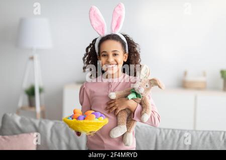 Mignon lapin de Pâques. Bonne fille noire tenant des œufs colorés lumineux dans un nid décoratif Banque D'Images