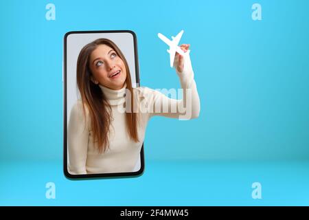 Voyage, concept de vacances. Une fille avec un avion de papier blanc sort de l'écran du smartphone. Une jeune femme est en ligne sur un téléphone portable. Banque D'Images