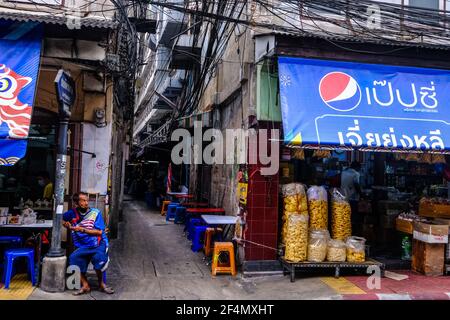 Un homme âgé se trouve à l'extérieur d'une boutique à côté de l'entrée d'une allée dans Chinatown, Bangkok, Thaïlande Banque D'Images