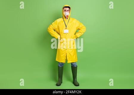 Photo pleine grandeur d'un jeune homme en imperméable et lunettes de protection porter un masque de protection contre le coronavirus isolé de couleur verte arrière-plan Banque D'Images