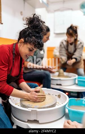 Photo de la bonne femme en tablier travaillant derrière une roue de potier dans un atelier. Banque D'Images