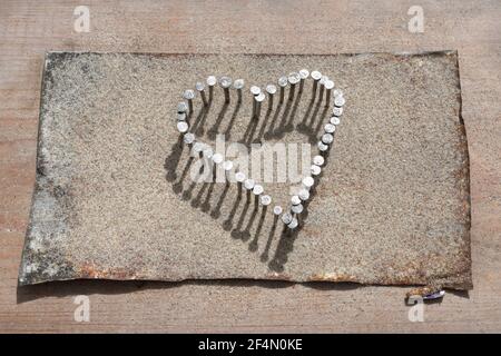 Coeur des clous martelé dans l'étain aplati sur la planche en bois et arrosé de sable de plage Banque D'Images