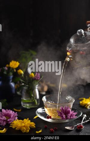 Préparation du thé, ambiance sombre. La vapeur du thé chaud est versée dans la bouilloire. Fleurs. Concept de plats chauds et sains Banque D'Images