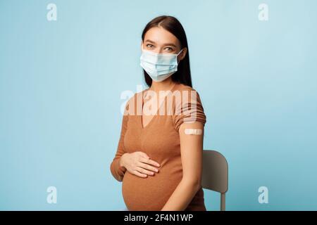 Femme enceinte vaccinée portant un masque de protection sur fond bleu Banque D'Images