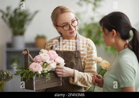Portrait de la taille vers le haut de la jeune femme donnant le bouquet au client tout en travaillant dans un fleuriste Banque D'Images