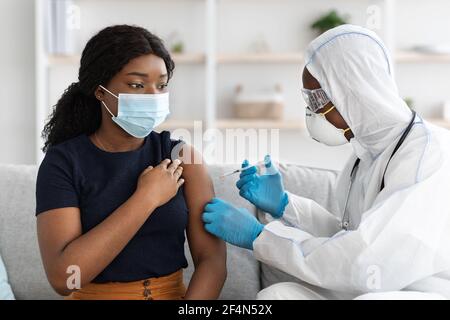 Femme noire dans le masque de visage se faire injecter à la maison Banque D'Images