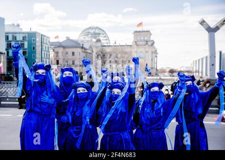 Berlin, Allemagne. 22 mars 2021. Les gens habillés comme des 'rebelles bleu' élèvent leurs poings sur le pont Marschall lors d'une représentation du mouvement de protection de l'environnement 'rébellion d'extinction' à l'occasion de la Journée mondiale de l'eau sous la devise 'protéger l'eau - arrêter la fracturation dans le monde entier'; le bâtiment Reichstag peut être vu en arrière-plan. Credit: Christoph Soeder/dpa/Alay Live News Banque D'Images