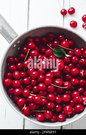 Cerises fraîches en passoire sur fond de bois blanc. Banque D'Images