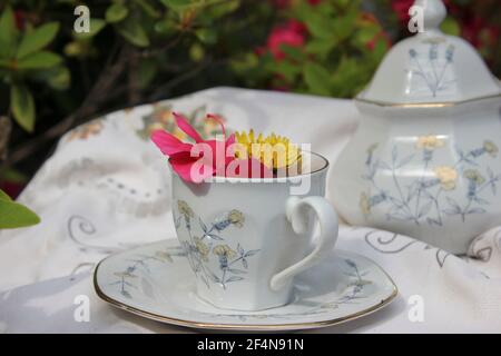 tasse en céramique blanche fine peinte avec des fleurs et entourée d'une bordure dorée au premier plan avec des fleurs à l'intérieur, en arrière-plan les coordonnées Banque D'Images