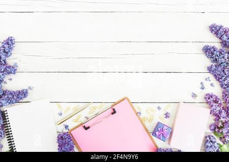 Presse-papiers, agenda, fleurs lilas et accessoires sur fond blanc en bois. Pose à plat Banque D'Images