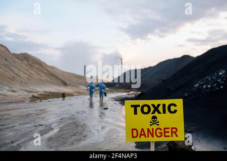 Panneau jaune avec annonce de zone toxique et dangereuse activée contexte de deux scientifiques contemporains en combinaison de protection bleue Banque D'Images