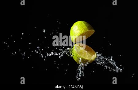 Des éclaboussures de jus d'un citron vert coupé sur fond noir. Banque D'Images