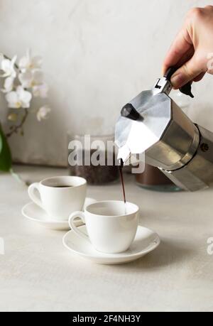 Le café est versé de la machine à café geyser dans la tasse à espresso. Concept de café du matin fraîchement préparé. Orientation verticale. Banque D'Images