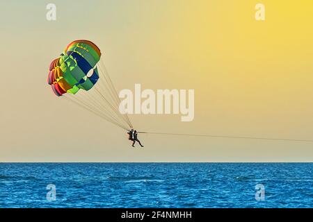 Les touristes hommes et femmes volent sur le parachute ascensionnel au-dessus de la mer sur fond du ciel et de l'horizon au coucher du soleil. Concept de vacances extrêmes. Banque D'Images