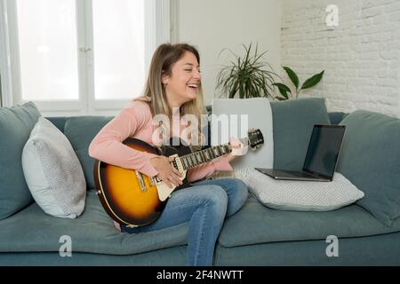 Femme jouant de la guitare électrique avec un ordinateur portable dans la leçon de musique en ligne. Femme s'amusant à regarder un didacticiel vidéo sur l'apprentissage de chansons rock. Loisirs et loisirs Banque D'Images