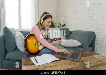 Musicienne attrayante femme jouant de la guitare électrique pendant un concert en ligne à la maison en isolement. Professeur de musique enseignement jouer instrument en ligne à l'aide de l Banque D'Images