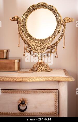 un miroir doré joliment décoré sur une table de chevet élégante. Élégance féminine, couleurs chaudes Banque D'Images