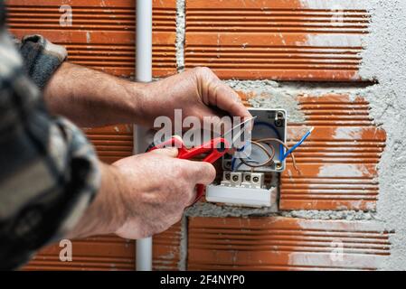 Un électricien au travail avec des ciseaux prépare les câbles électriques d'un système électrique résidentiel. Industrie de la construction. Banque D'Images