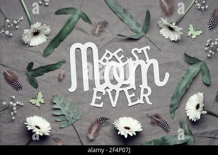 Carte de vœux de fête des mères. Lit à plat floral jungle sur le linge en tissu. Texte papier meilleur maman jamais. Mélange de plantes tropicales - feuilles de fougères exotiques, fleurs de gerbera Banque D'Images
