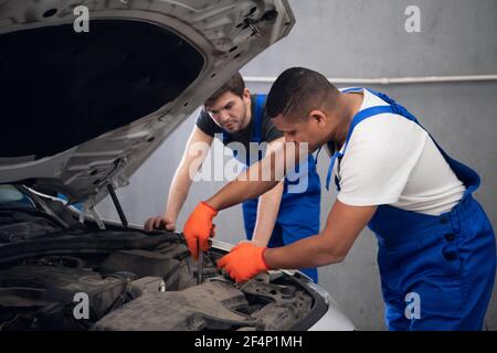 Ouvriers d'atelier inspectant le capot d'une voiture Banque D'Images