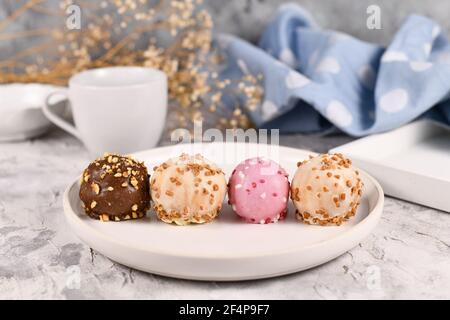 Petites boules de gâteau colorées émaillées de chocolat blanc, rose et brun avec saupoudrer sur une assiette blanche Banque D'Images