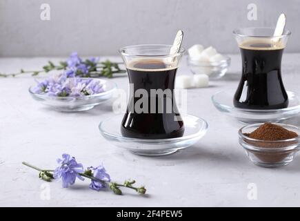 Boisson chicorée dans deux tasses en verre, avec concentré et fleurs sur fond gris. Boisson saine à base de plantes, succédané de café Banque D'Images