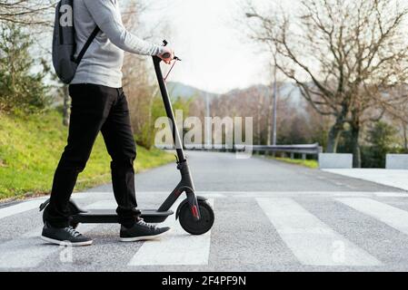 Crop man avec scooter électrique marchant sur le passage de côté Banque D'Images