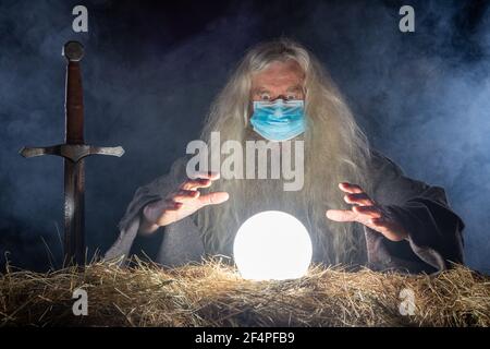 L'ASSISTANT AVEC MASQUE CORONA REGARDE DANS LA BOULE DE CRISTAL PRÉDIRE L'AVENIR Banque D'Images