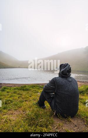 Homme méconnaissable devant un lac de volcan assis regardant autour Banque D'Images